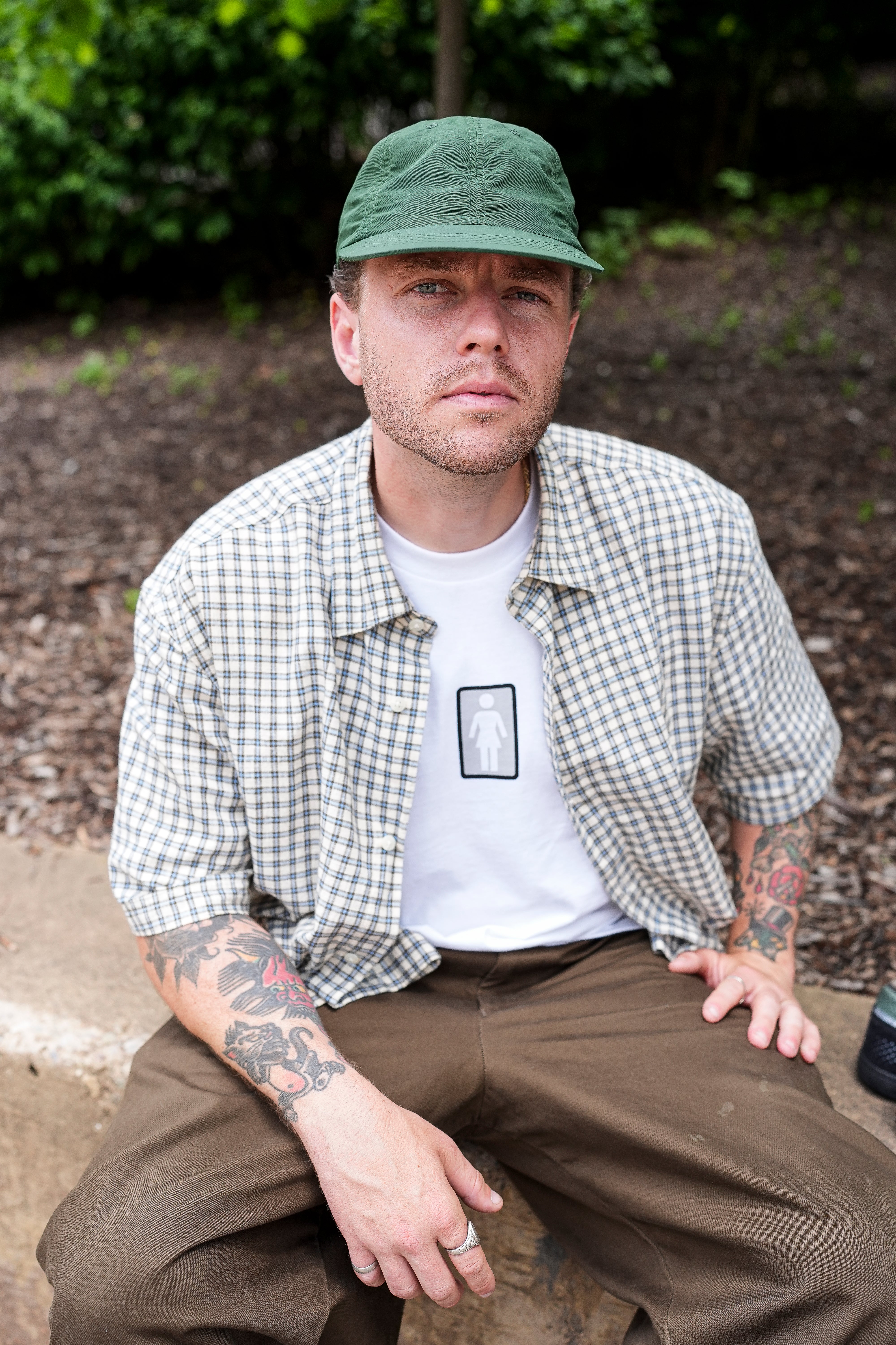 Man wearing a green cap and checkered shirt sitting outdoors.