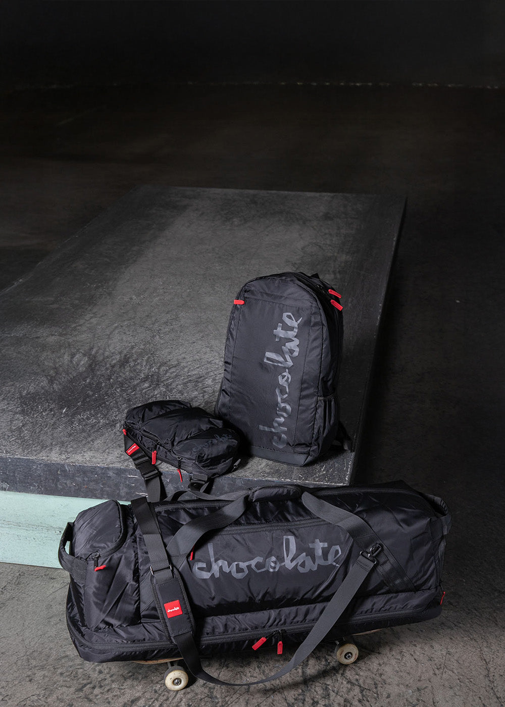 Black duffel bag and backpack with 'Chocolate' branding on a dark surface.